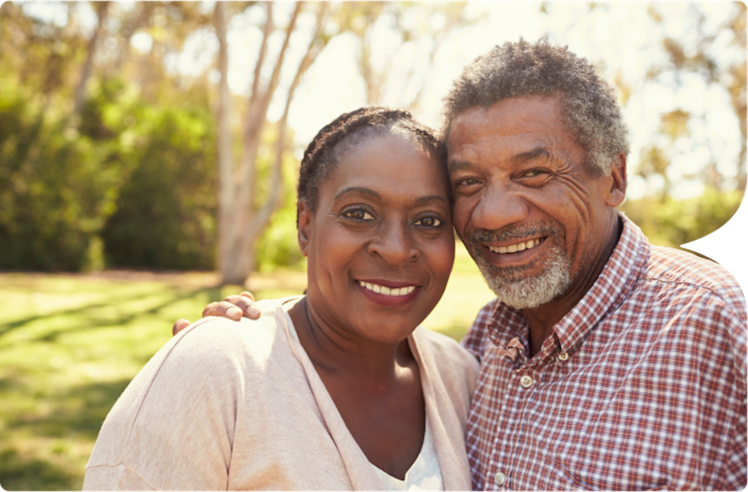 Photograph of an older African American Couple standing outside by some trees.