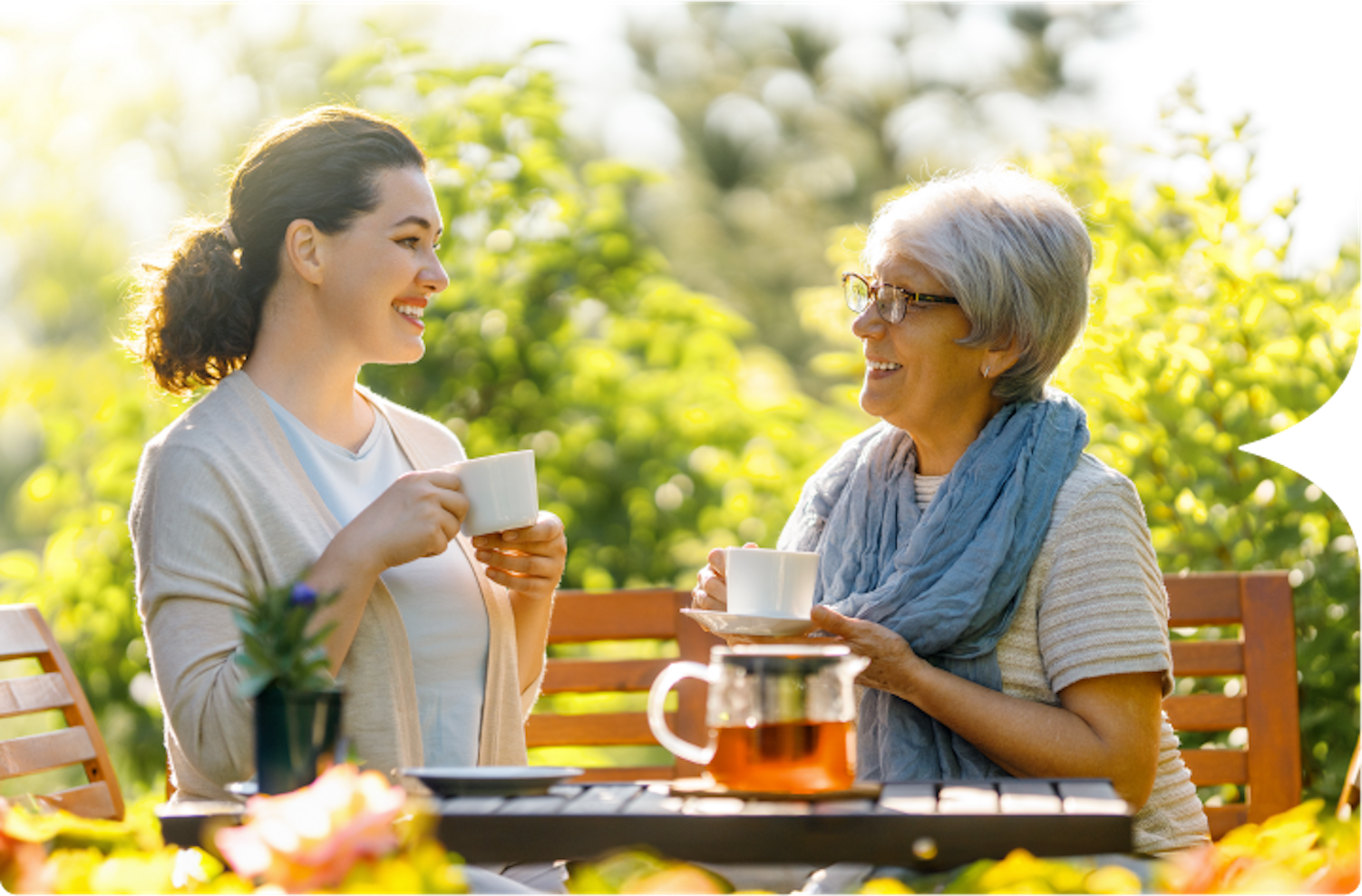 Photograph of a young Caucasian woman having tea outside with an older Caucasian woman.